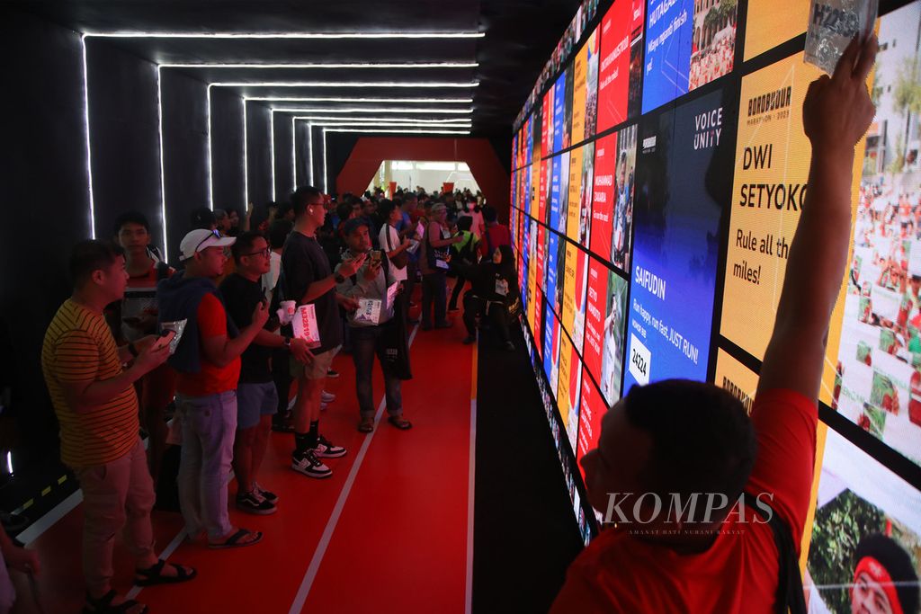 Peserta berfoto dengan latar belakang papan layar digital yang menunjukkan daftar peserta lari pada hari kedua pengambilan<i> race pack </i>atau perlengkapan pelari Borobudur Marathon 2023 di Hotel Artos, Kota Magelang, Jawa Tengah, Sabtu (18/11/2023). 