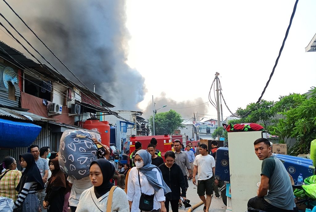 Warga hilir mudik membawa barang dan menjauhi asap pekat hitam yang menyelimuti permukiman warga di RW 003 Jalan Kapuk Utara 2, Kapuk Muara, Penjaringan, Jakarta Utara, yang ludes terbakar, Minggu (30/7/2023).