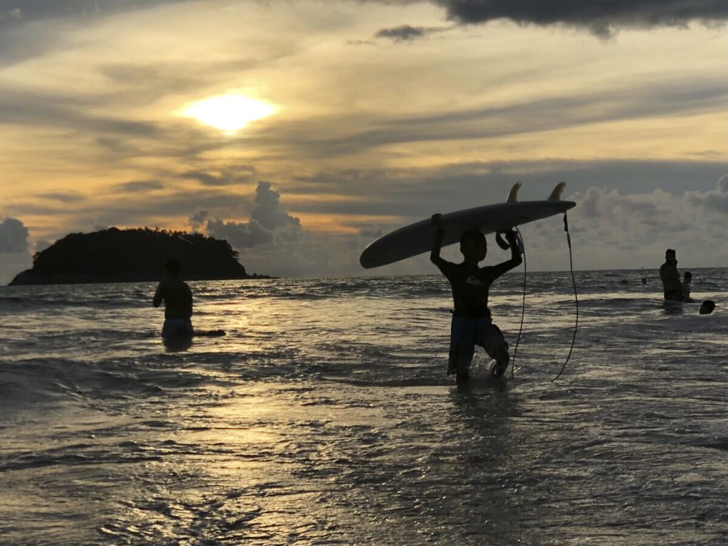 Peselancar membawa papan selancar saat matahari tenggelam di Pantai Kata, Phuket, Thailand, 26 Mei 2019. 