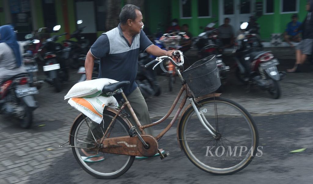 Warga mendorong sepeda seusai pembagian bantuan pangan beras di Balai Desa Ketajen, Kecamatan Gedangan, Sidoarjo, Jawa Timur, Jumat (15/3/2024). Bantuan tersebut sangat membantu warga di tengah melonjaknya harga bahan pokok.  
