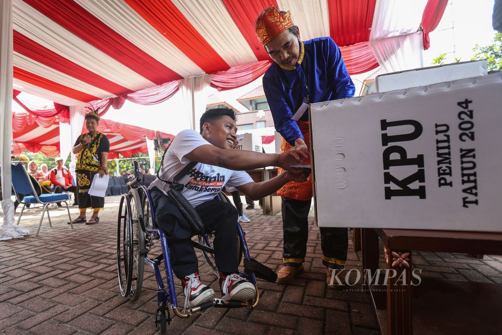 Pemilih disabilitas memasukkan surat suara dibantu Panita Pemungutan Suara saat simulasi pemungutan suara Pemilu 2024 di halaman Kantor Wali Kota Jakarta Pusat, Rabu (17/1/2024). Komisi Pemilihan Umum Jakarta Pusat menggelar simulasi pemungutan dan penghitungan suara di tempat pemungutan suara. 