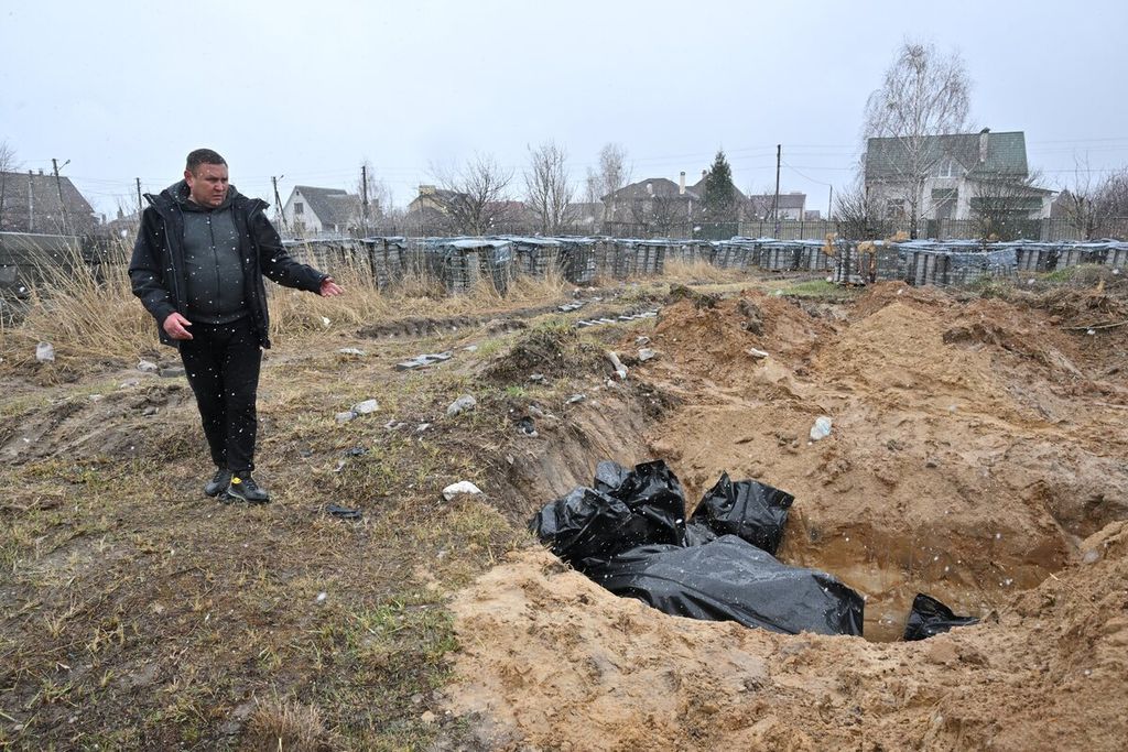 Seorang pria menunjuk kuburan massal di kota Bucha, barat laut ibu kota Ukraina Kyiv, Minggu (3/4/2022). Ukraina dan negara-negara Barat menuduh pasukan Rusia melakukan kejahatan perang dan mengeksekusi warga sipil setelah penemuan kuburan massal itu.  