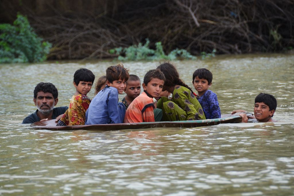 Seorang pria (kiri) bersama seorang pemuda menggunakan parabola memindahkan anak-anak melintasi daerah banjir setelah hujan lebat di Distrik Jaffarabad, Provinsi Balochistan, pada 26 Agustus 2022. 