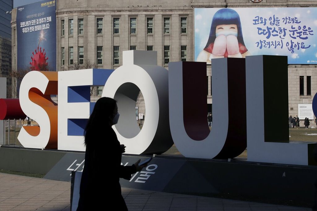 Seorang wanita yang mengenakan masker berjalan di dekat logo penanda ibu kota Korea Selatan, Seoul. 