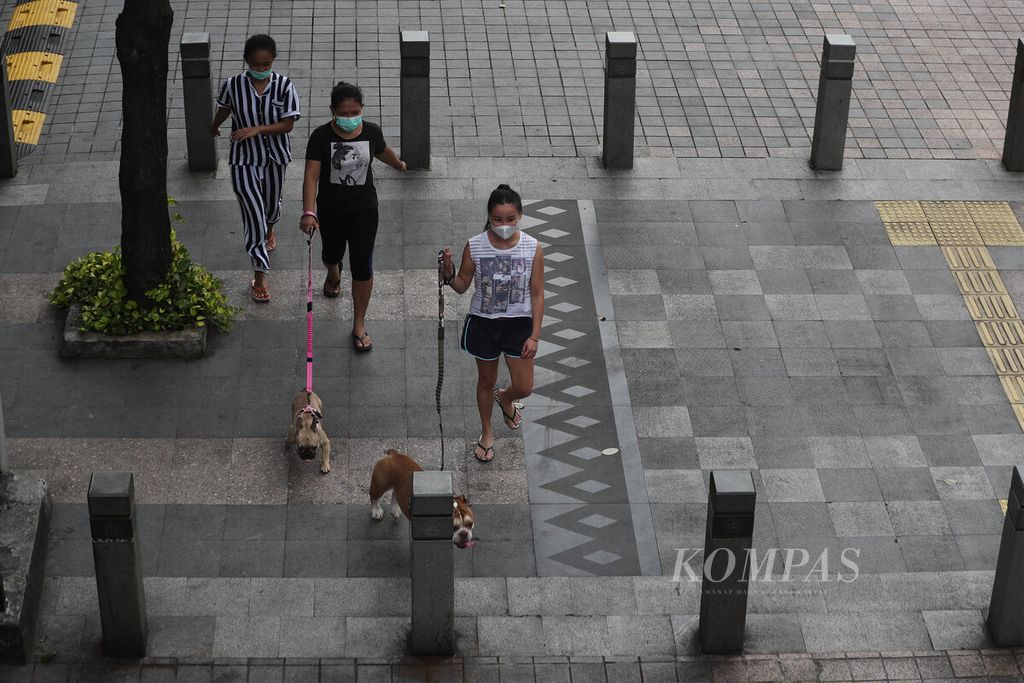 Warga bersama anjing peliharaannya menyusuri trotoar di Jalan Jenderal Sudirman, Jakarta Selatan, yang lengang karena pemberlakuan PPKM darurat, Rabu (21/7/2021). 