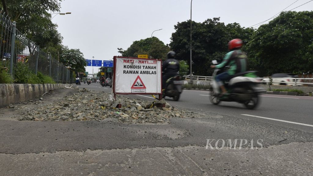 Rambu peringatan terpasang di salah satu sisi jalan yang rusak di Jalan S Parman, Jakarta Barat, Kamis (16/1/2020).