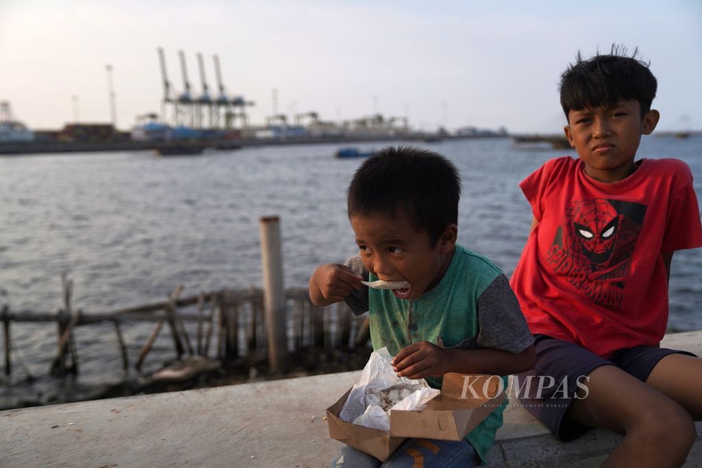 Anak-anak makan nasi kotak yang dibagikan oleh mobil keliling di perkampungan nelayan Kalibaru, Cilincing, Jakarta Utara, Jumat (22/12/2023).