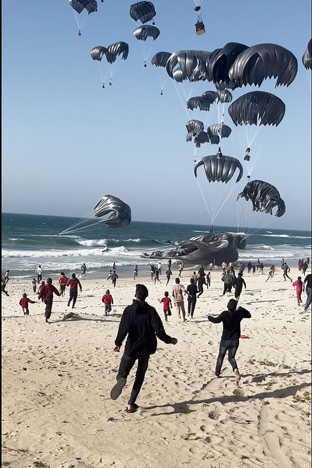 Potongan gambar video AFPTV memperlihatkan warga Palestina berlarian saat bantuan bahan makanan dijatuhkan dari udara di pantai Gaza, Sabtu (2/3/2024).  