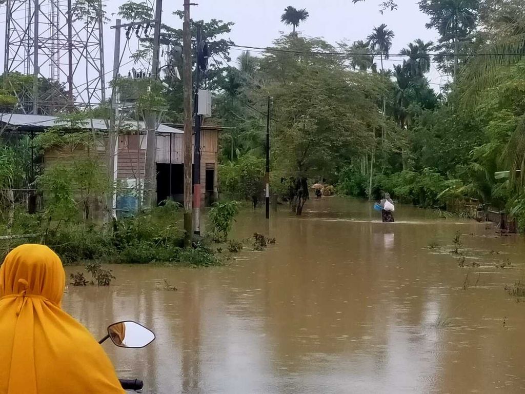 Warga melintasi jalan Desa Meuria, Kecamatan Matang Kuli, Kabupaten Aceh Utara, Provinsi Aceh, Sabtu (8/10/2022), yang digenangi banjir. Banjir di Aceh Utara setidaknya menggenangi 142 desa di 14 kecamatan. Banjir terjadi setelah beberapa sungai utama di kabupaten itu meluap karena tidak mampu menampung tambahan debit air.