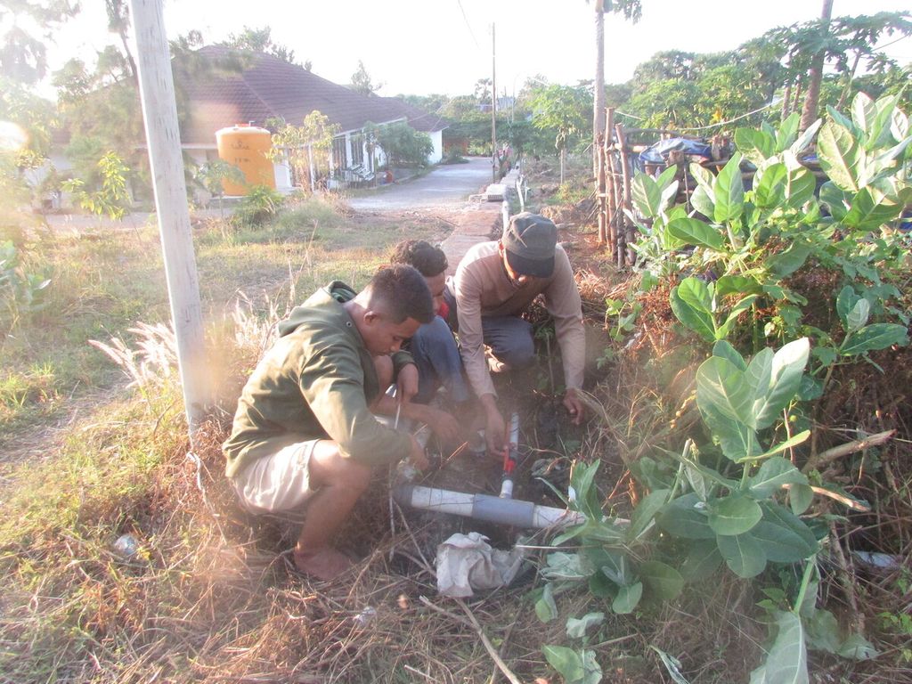 Prof Nyoman Mahayasa (topi) dibantu dua mahasiswa Faperta Undana Kupang, Selasa (14/6/2022), memperbaiki pipa air yang rusak. Pipa ini bermanfaat mengalirkan air dari tendon ke bak penampungan kemudian dialirkan ke setiap tanaman dengan sistem irigasi tetes.