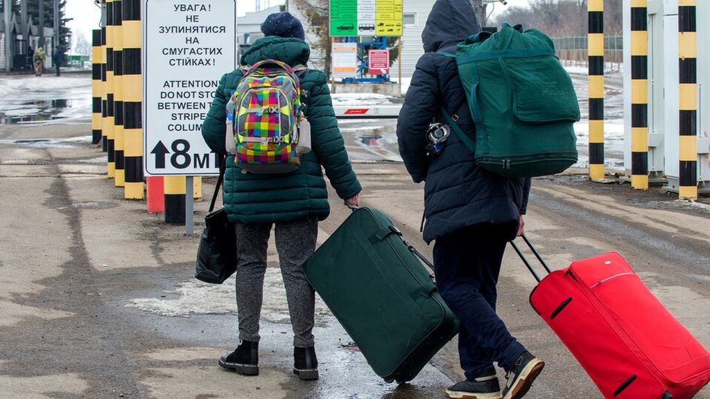 Orang-orang membawa koper dan bawaan mereka saat berjalan ke sisi Rusia di pos pemeriksaan perbatasan Ukraina-Rusia, sekitar 40 km dari kota terbesar kedua di Ukraina, Kharkiv, Rabu (16/2/2022).  (Photo by Sergey BOBOK / AFP)