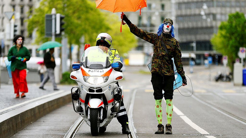 Seorang pengunjuk rasa, yang mengenakan kostum badut memegang payung, memayungi polisi bersepeda motor saat berlangsung unjuk rasa memperingati Hari Buruh Internasional, di Zurich, Swiss, Senin (1/5).