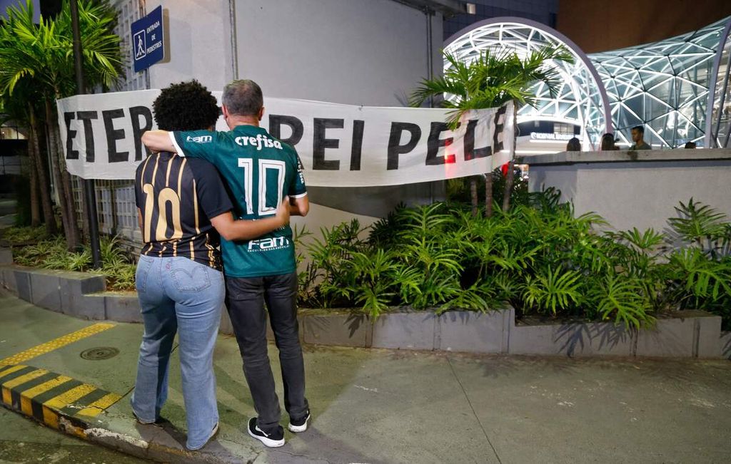 Penggemar sepak bola menatap spanduk bertuliskan "Raja Pele Abadi" di luar Rumah Sakit Albert Einstein, Sao Paulo, setelah mendengar kabar wafatnya legenda sepak bola Brasil Pele, Kamis (29/12/2022). 