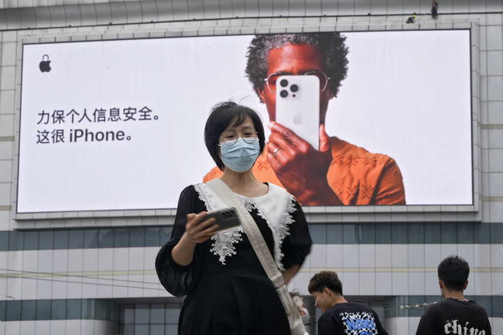 Seorang perempuan memegang ponselnya saat berjalan melewati layar iklan Apple iPhone bertuliskan aga keamanan informasi pribadi Anda. Ini sangat iPhone di Beijing, China, Rabu, 24 Mei 2023.