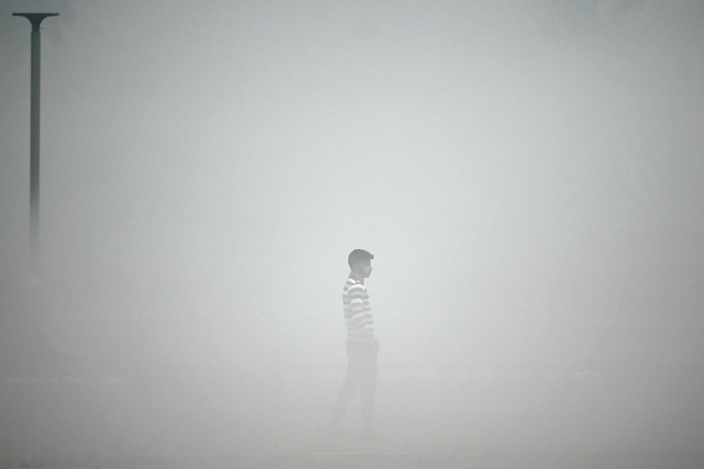 Seorang pejalan kaki melintas di tengah pekatnya kabut polusi udara di New Delhi, Senin (13/11/2023). 