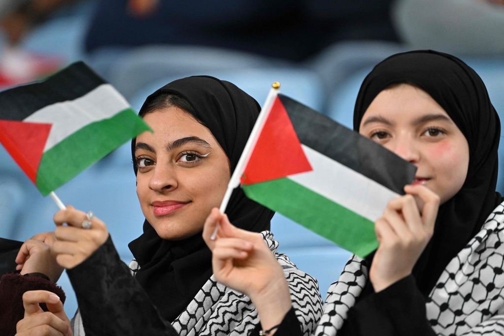 Pendukung mengibarkan bendera Palestina saat menonton laga Palestina melawan UEA, Kamis (18/1/2024). 