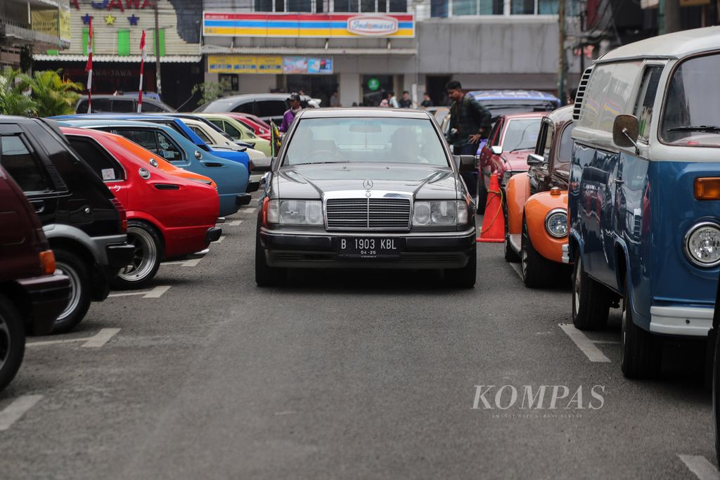 Mobil Mercedes Benz 300e melintas di antara mobil tua yang terparkir di kawasan Blok M, Jakarta, Sabtu (29/7/2023). Puluhan sepeda motor dan mobil tahun 1980 sampai 1990-an mengikuti parade ini. Parade ini mengelilingi Melawai Plaza. Acara ini merupakan rangkaian dari acara Lintas Melawai yang diadakan di Blok M. 