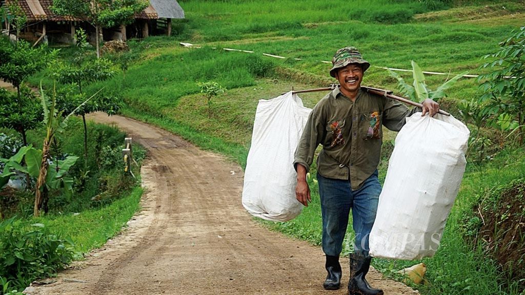 Seorang petani tersenyum saat melintasi jalan desa dari lahan pertaniannya di Kampung Gandok, Desa Suntenjaya, Lembang, Kabupaten Bandung Barat, Jawa Barat, Selasa (29/1/2019). Jalan keras ini membantu petani mengakses lahan pertanian dan pemasaran.
