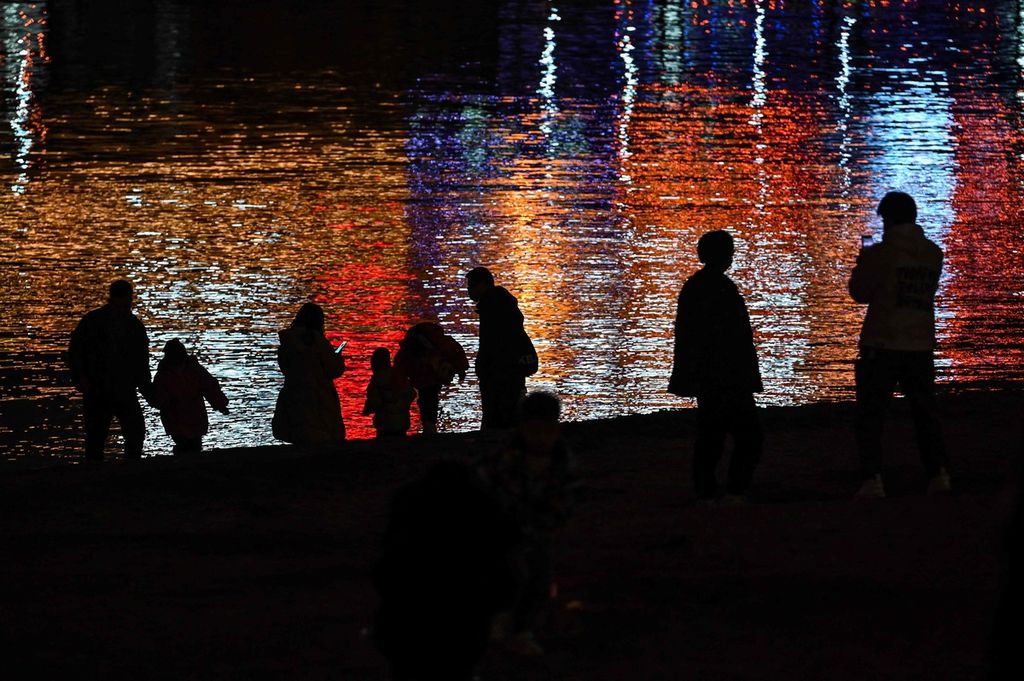 Siluet warga Wuhan menjadi latar depan pantulan cahaya lampu gedung-gedung bertingkat di permukaan Sungai Yangtze, Jumat (20/1/2023) menjelang perayaan tahun baru Imlek.