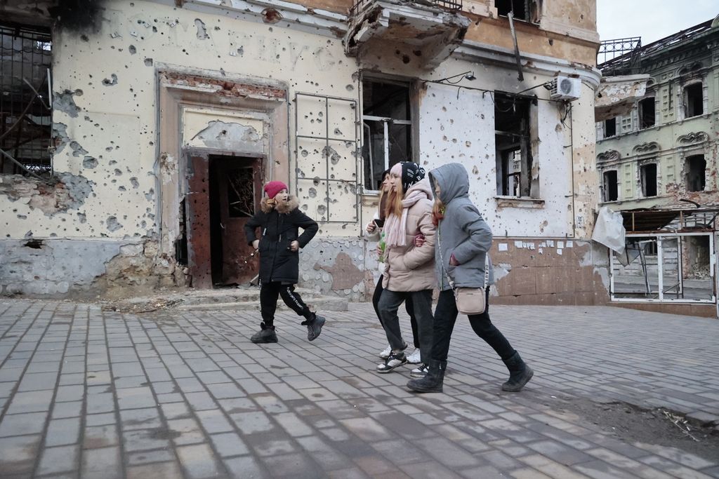 Sekelompok remaja berjalan menyusuri jalan di kompleks bangunan apartemen yang rusak di Mariupol, Ukraina, Sabtu (25/2/2023). 