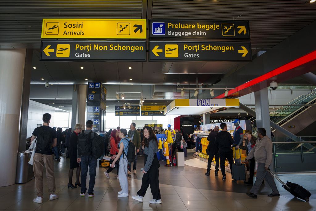 Para penumpang melintas di bawah papan informasi yang mengarahkan penumpang salah satunya ke jalur gerbang menuju Schengen di Bandar Udara Internasional Henri Coanda di Otopeni, dekat Bucharest, Romania, 28 Maret 2024. 