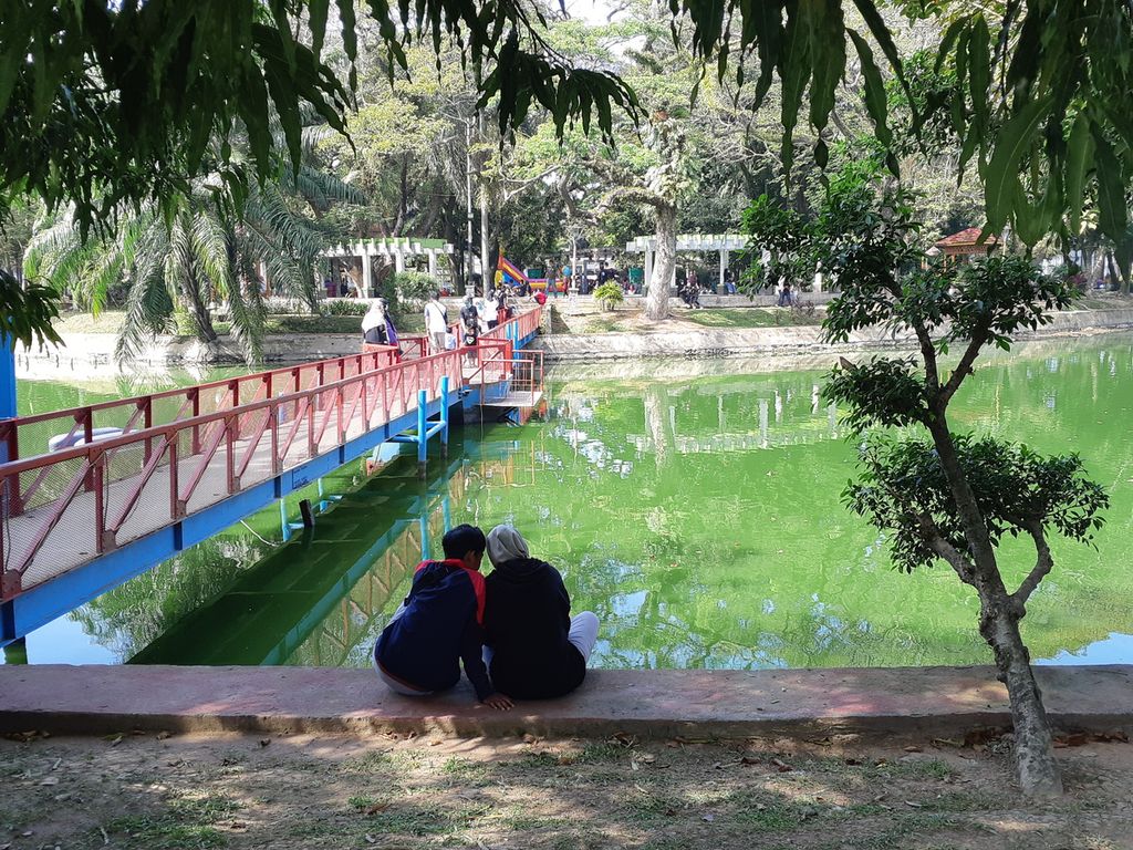 Dua pengunjung duduk di pinggir danau kawasan Taman Kota Kambang Iwak, Palembang, Sumatera Selatan, Minggu (13/6/2021). Keberadaan taman kota bukan sekadar tempat rekreasi,  melainkan menjadi wajah kota itu sendiri.