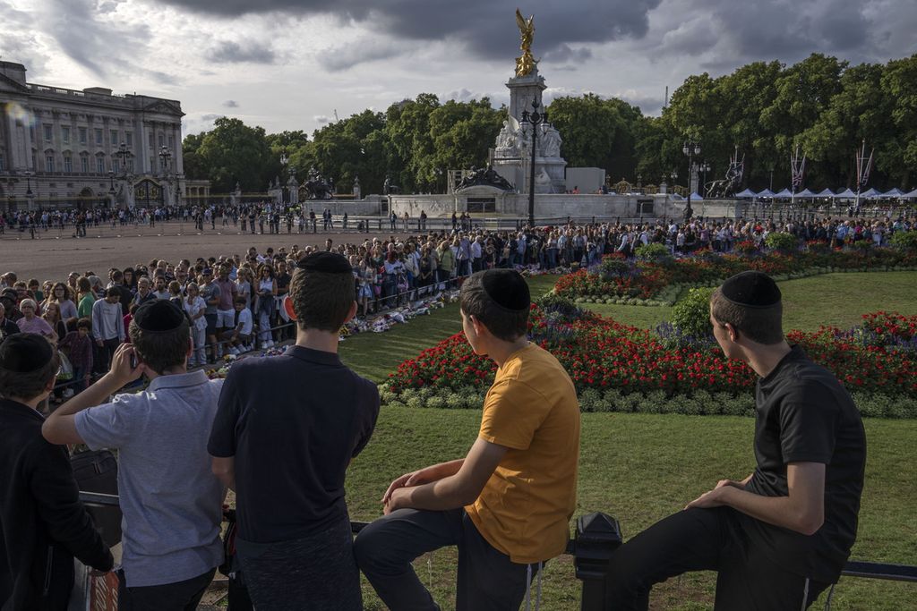 Beberapa anak muda menyaksikan antrean panjang warga yang ingin meletakkan bunga untuk mendiang Ratu Elizabeth II di depan Istana Buckingham, London, Inggris (11/9/2022). 