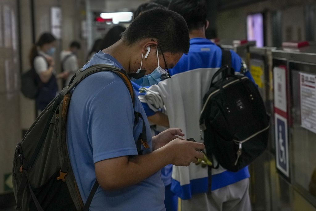 Seorang remaja asyik melihat layar gawai pintarnya sambil menunggu kedatangan kereta bawah tanah di Beijing, Selasa (14/9/2021). Pada Agustus 2023, CAC kembali mengusulkan pengetatan akses internet bagi remaja dan anak di bawah umur untuk mengatasi kecanduan gim atau layanan <i>video streaming</i>. 