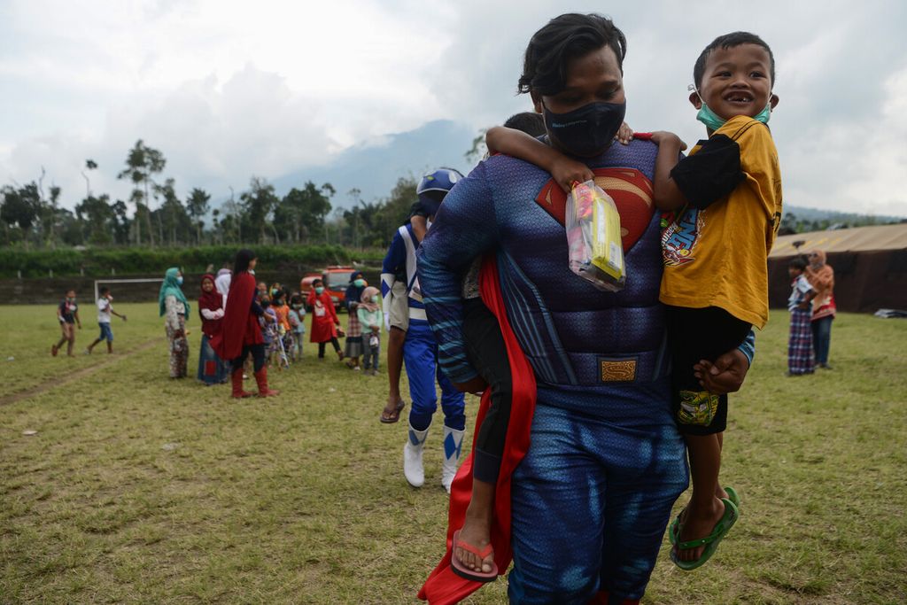 Sukarelawan yang tergabung dalam Komunitas Superhero Mendongeng dan Membaca Keliling bermain dengan menggendong anak-anak pengungsi di tempat pengungsian Desa Klakah, Selo, Boyolali, Jawa Tengah, Sabtu (21/11/2020). 
