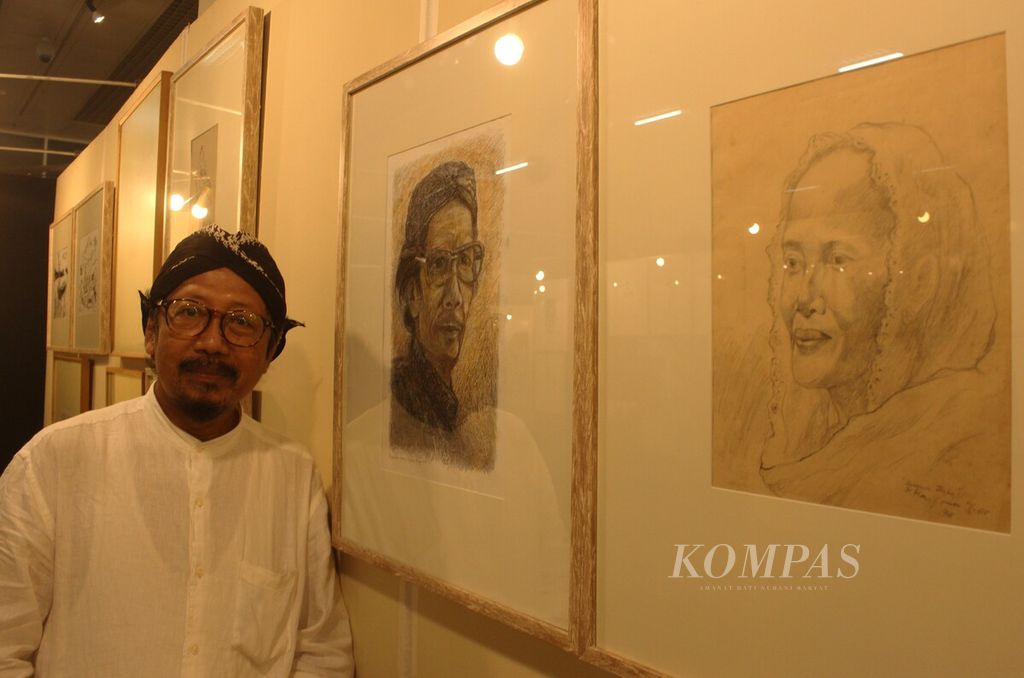 Perupa, penyair, sekaligus jurnalis Yusuf Susilo Hartono berdiri di samping sketsa wajah orangtuanya dalam Pameran Retrospeksi 40 Tahun Berkarya Among Jiwo di Museum Nasional Indonesia, Jakarta, Kamis (10/11/2022).
