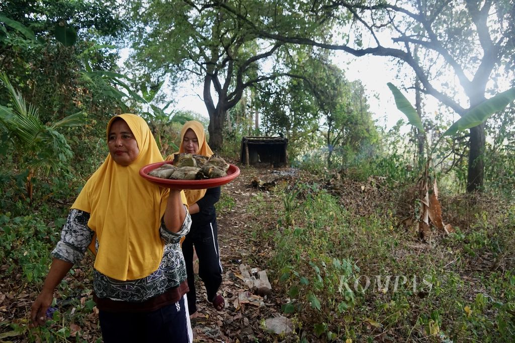 Wa Mari (42) dan Wa Masrida (45) membawa hasil bakar batu berupa olahan ubi, singkong, dan pisang, di Desa Pajam, Kaledupa Selatan, Wakatobi, Sulawesi Tenggara, Selasa (29/8/2023). Tombole adalah hasil olahan pangan lokal dengan proses bakar batu.