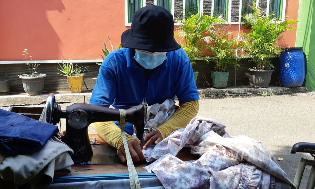 Roni (47) sedang menjahit seprei yang robek milik pelanggannya di sebuah perumahan di kawasan Legoso, Ciputat Timur, Tangerang Selatan, Banten, Selasa (21/9/2021). Penjahit keliling ini memperoleh pendapatan sekitar Rp 100.000 per hari.