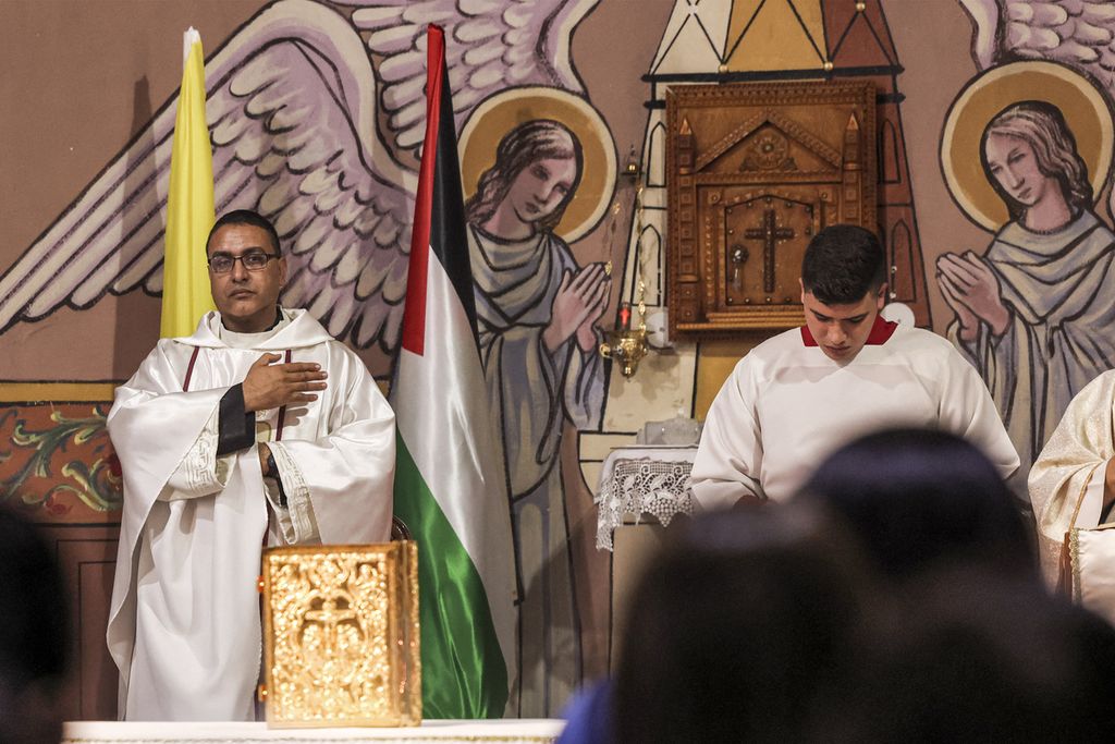 Salah satu pemimpin misa berdiri di dekat bendera Palestina dan bendera Takhta Suci dalam Misa Malam Natal, di Gereja Katolik Roma Keluarga Kudus, di Gaza City, 24 Desember 2022. 