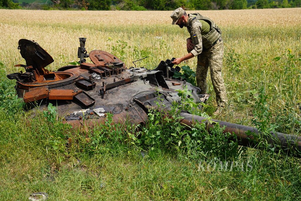 Anggota militer Ukraina memeriksa bagian tank milik Rusia yang hancur di sebuah ladang gandum di Desa Mala Rohan, Provinsi Kharkiv, Ukraina, Selasa (5/7/2022). Banyak bahan peledak ataupun ranjau yang belum dijinakkan tersebar di ladang pertanian warga.