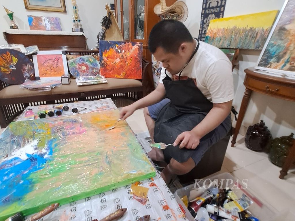 Diego Luister Berel (22), pelukis dengan <i>down syndrome</i>, tengah berkreasi di rumahnya di Jakarta, Kamis (25/5/2023). Salah satu karyanya, "Balinese Penjor", memenangi kompetisi seni rupa bertema Artfusion di Pameran The Holy Art Gallery, London, pada Maret 2022.