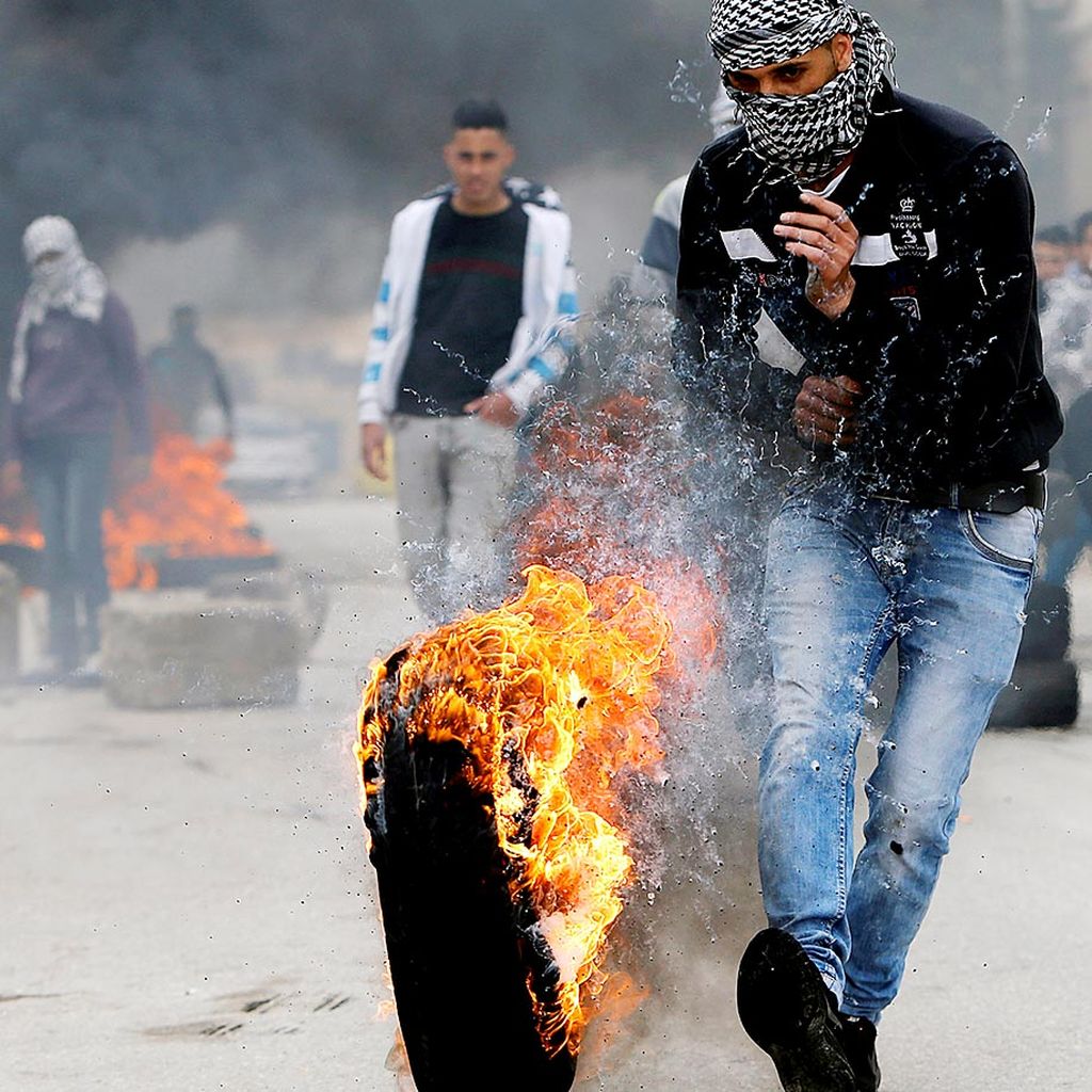 Seorang pemuda  Palestina menendang sebuah ban terbakar dalam unjuk rasa yang mengiringi bentrokan dengan tentara Israel di  Halhoul, di wilayah pendudukan di Tepi Barat, Sabtu (17/2).