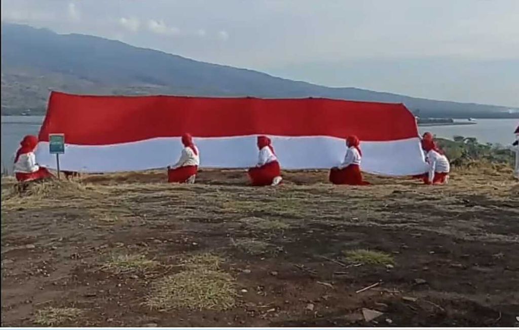 Di Lombok, NTB, para ibu anggota Sekolah Perempuan dengan berpakaian merah dan putih memperingati Hari Kemerdekaan Ke-77 RI, Rabu (17/8/2022), dengan menggelar upacara membentangkan bendera Merah Putih berukuran besar di atas Bukit Kayangan dengan latar belakang laut.