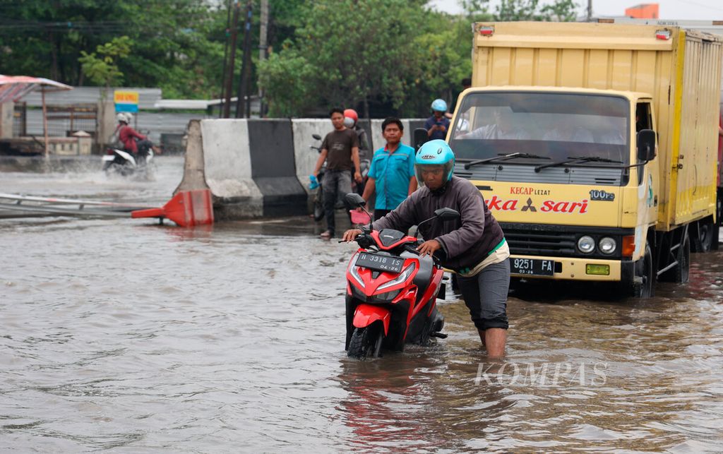 Warga mendorong sepeda motornya yang mogok saat melintasi banjir di Kaligawe, Kota Semarang, Jawa Tengah, Selasa (27/11/2023). 