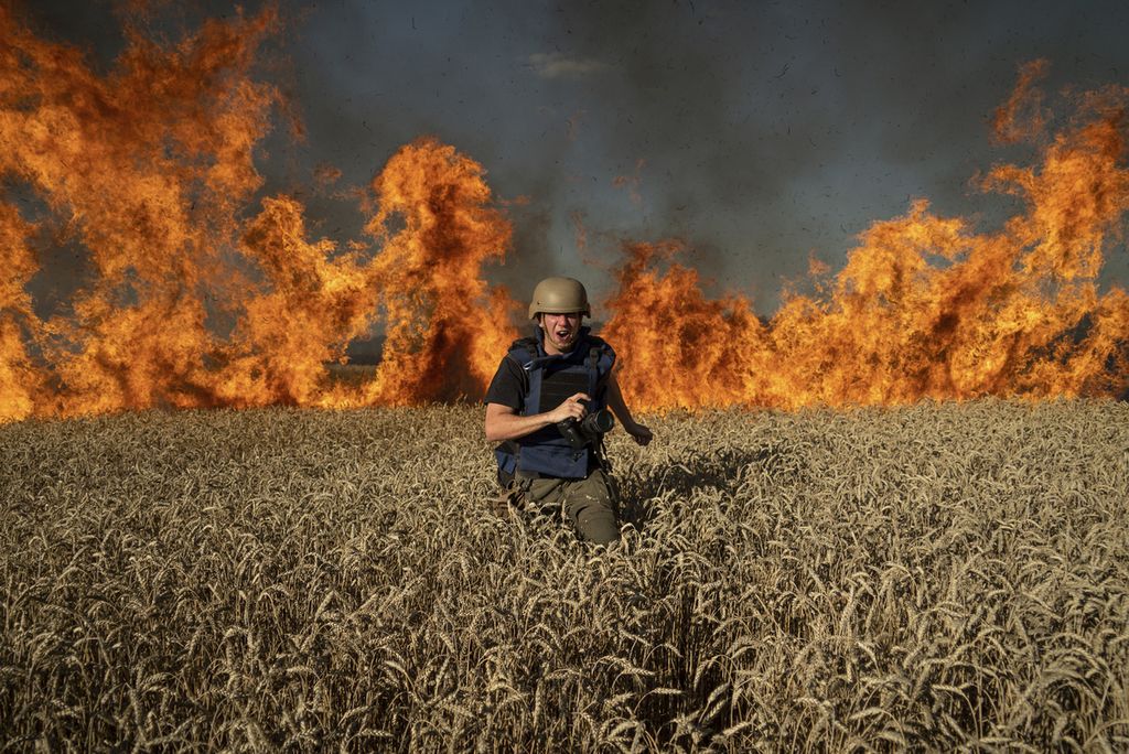 Seorang jurnalis foto, Evgeniy Maloletka, berlari menghindari ladang gandum yang terbakar di wilayah Kharkiv, Ukraina, Jumat (29/7/2022). Pemerintah Rusia, Sabtu (29/10/2022) memutuskan mundur dari Kesepakatan Laut Hitam yang memungkinkan Ukraina bisa mengekspor gandum dan produk biji-bijian mereka.