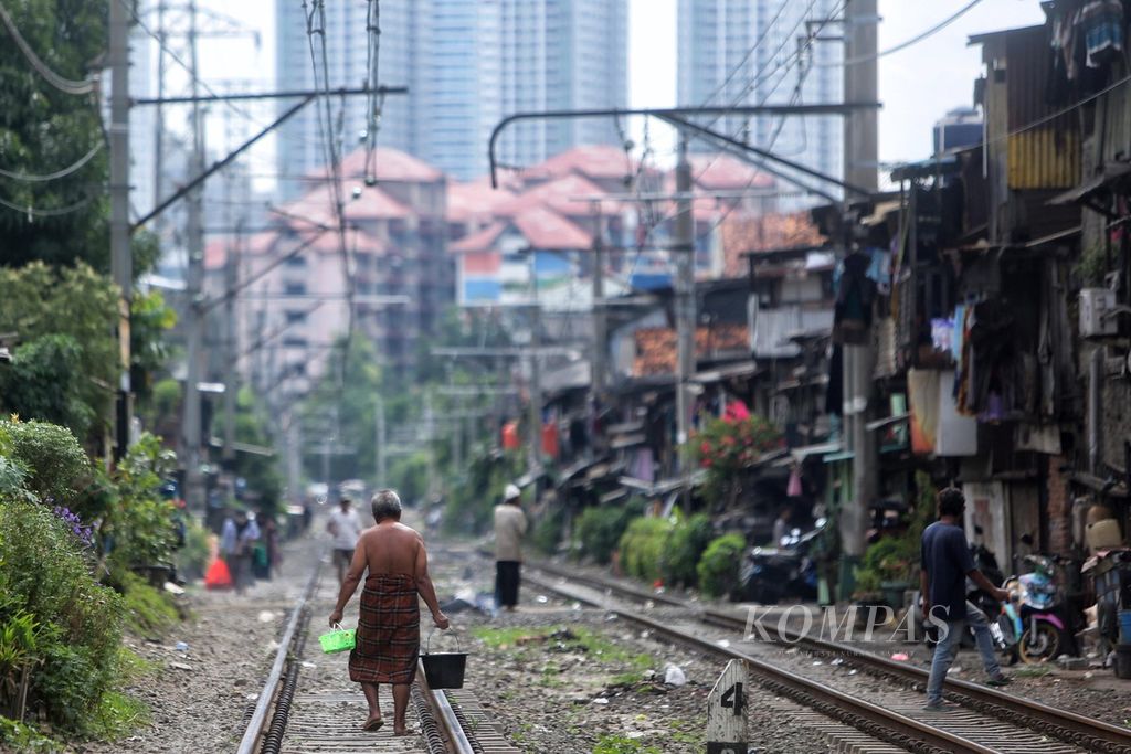 Warga menyusuri rel menuju tempat mandi umum di permukiman padat penduduk di tepi jalur KRL, Petamburan, Jakarta Pusat, Kamis (25/3/2021). Berdasarkan data Badan Pusat Statistik, tingkat kemiskinan Indonesia per September 2020 sebesar 10,19 persen atau 27,55 juta orang. 