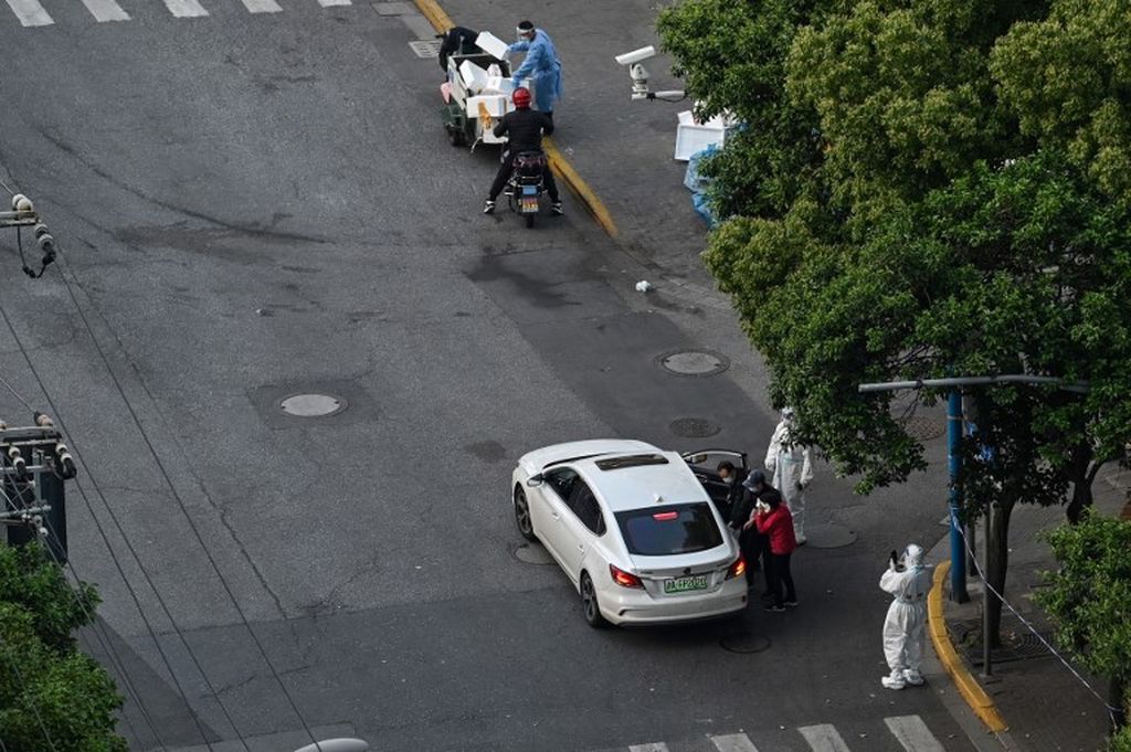 Seorang polisi (kanan bawah) mengenakan alat pelindung diri (APD) berdiri di sisi jalan sementara warga (tengah) masuk ke mobil selama penguncian virus Covid-19 di distrik Jing'an di Shanghai, Kamis (5/5/2022). 