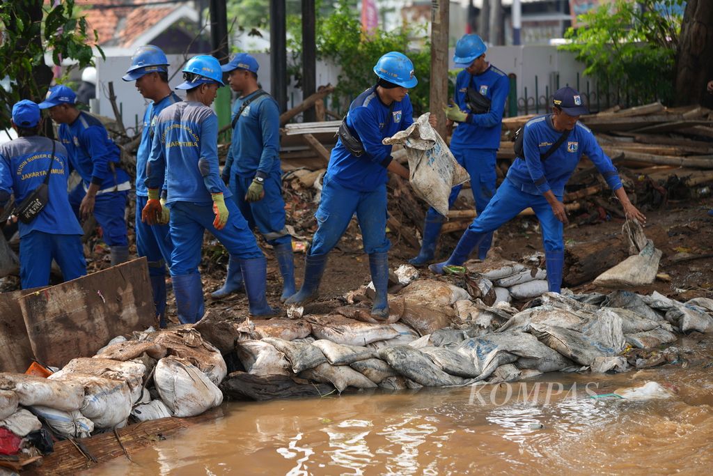 Petugas Suku Dinas Sumber Daya Air saat menangani Tanggul Kalibaru yang jebol di Simpang HEK, Kramat Jati, Jakarta Timur, Senin (25/3/2024).