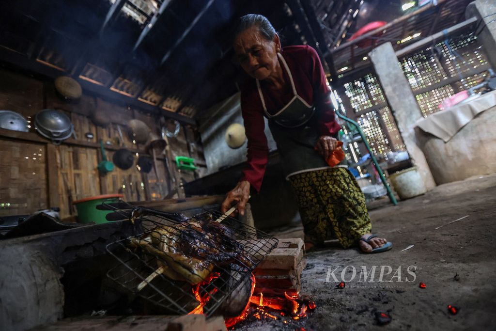 Mbah Ning (78) membakar ayam untuk masakan pecel <i>pithik </i>di Desa Kemiren, Kabupaten Banyuwangi, Jawa Timur, untuk acara selamatan pada Sabtu (18/11/2023). Pecel <i>pithik</i> merupakan menu ritual yang harus dimasak oleh perempuan yang telah menopause.