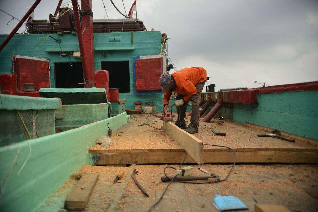 Seorang pekerja merapikan kayu untuk menambal bagian kapal yang telah rusak di Pelabuhan Perikanan Samudera Nizam Zachman, Muara Baru, Jakarta Utara, Selasa (3/1/2023). Akibat cuaca buruk, sejumlah nelayan di Pelabuhan Perikanan Samudera Nizam Zachman berhenti melaut. 
