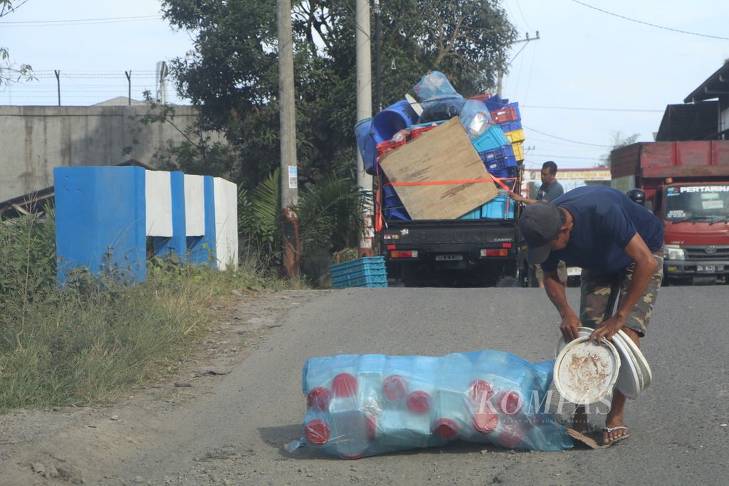 Sopir angkutan truk mengambil barang yang terjatuh dari truknya yang kelebihan muatan dan dimensi di jalan akses ke Jalan Tol Belawan-Medan-Tanjung Morawa di Kabupaten Deli Serdang, Sumatera Utara, Sabtu (7/1/2023).