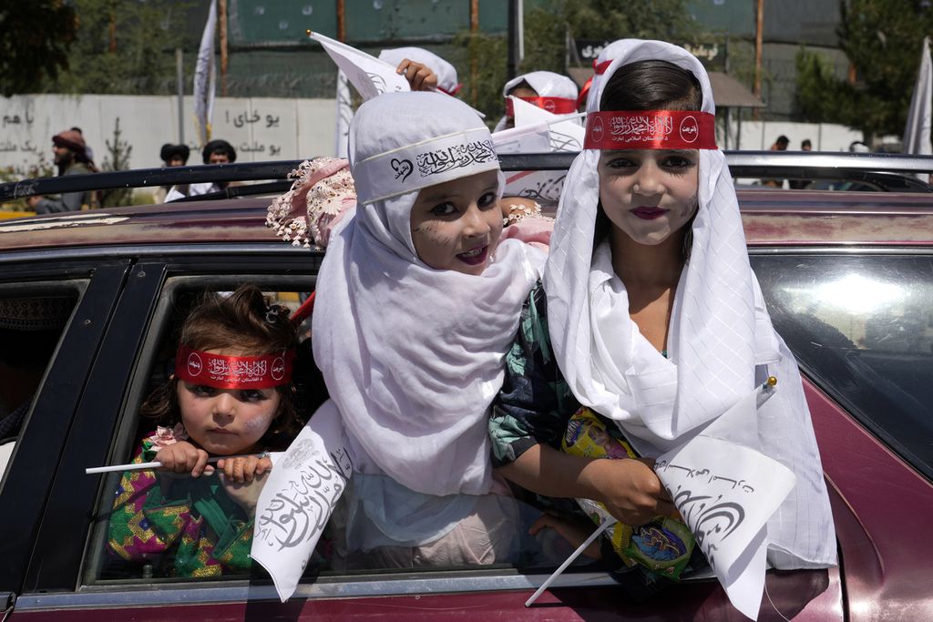 Anak-anak memegang bendera Taliban saat perayaan satu tahun penarikan pasukan pimpinan AS dari Afghanistan di depan Kedutaan Besar AS di Kabul, Afghanistan, Rabu )31/8/2022).
