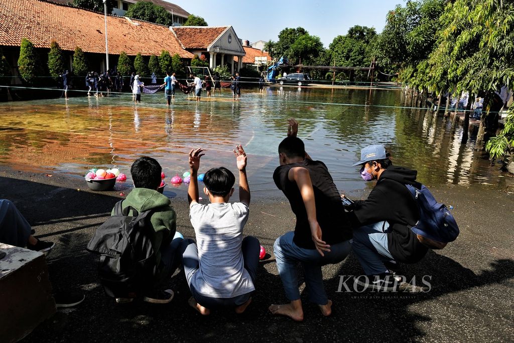 Siswa SMAN 4 Tangerang Selatan, Banten, bermain genangan air hujan di halaman sekolah, Jumat (10/6/2022). Genangan air itu sudah lebih dari seminggu tidak surut. Adanya tumpukan sampah dari TPS ilegal yang berada tak jauh dari sekolah itu diduga sebagai sumber penyebab air tak juga surut.