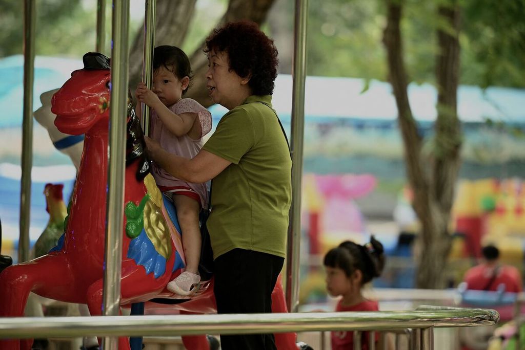 Seorang perempuan menemani anaknya naik komidi putar di sebuah taman di Beijing, 2 Agustus 2022. Jumlah penduduk China akan menurun mulai 2025 karena banyak perempuan enggan punya anak.  