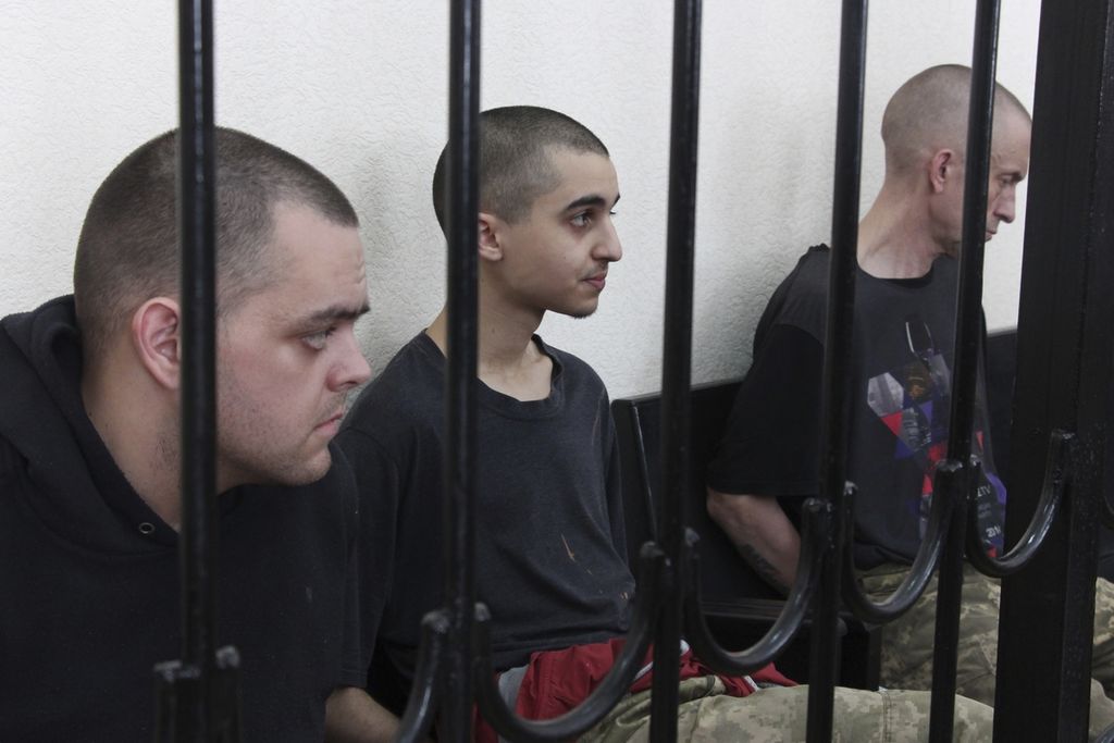 Dua warga Inggris, Aiden Aslin (kiri), dan Shaun Pinner (kanan), serta warga Maroko, Saadun Brahim (tengah), duduk di dalam sel di ruang pengadilan di Donetsk, yang berada di bawah kontrol Pemerintahan Republik Rakyat Donetsk, di wilayah timur Ukraina, Kamis (9/6/2022). 