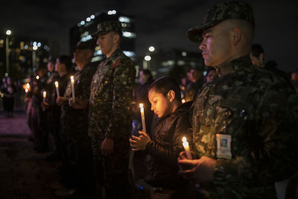 Seorang anak laki-laki memegang sebatang lilin saat malam tirakatan mengenang tentara yang gugur dalam pertempuran dengan kelompok bersenjatan FARC, di Bogota, Kolombia pada Jumat (9/12/2022).